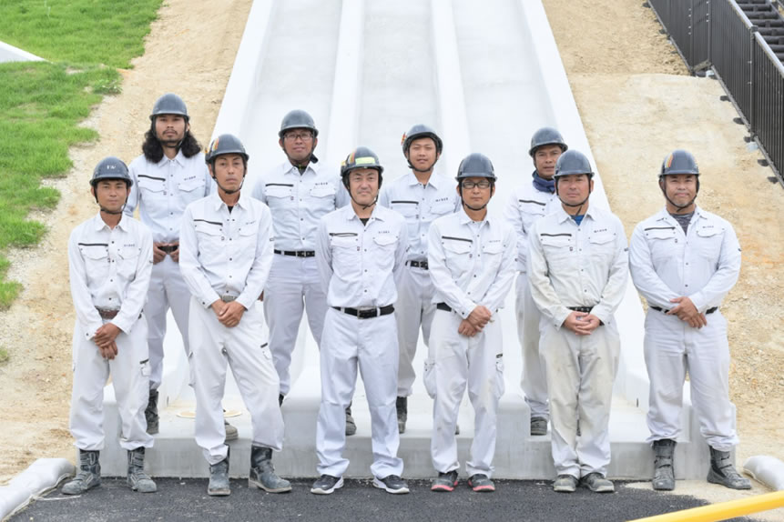 作業現場で、男性達がヘルメットを持って並んでいる